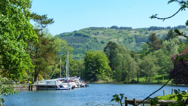 A lakeside view with boats docked at a pier, surrounded by lush greenery and hills. - Maple - Woodland Cottages (Windermere)