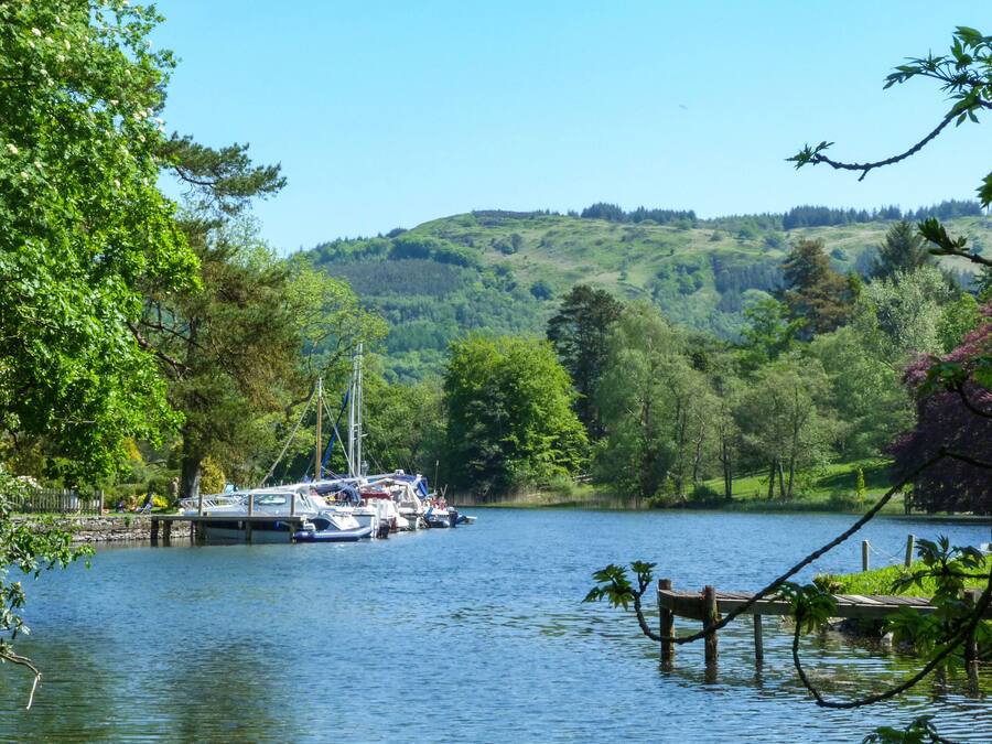 A lakeside view with boats docked at a pier, surrounded by lush greenery and hills.