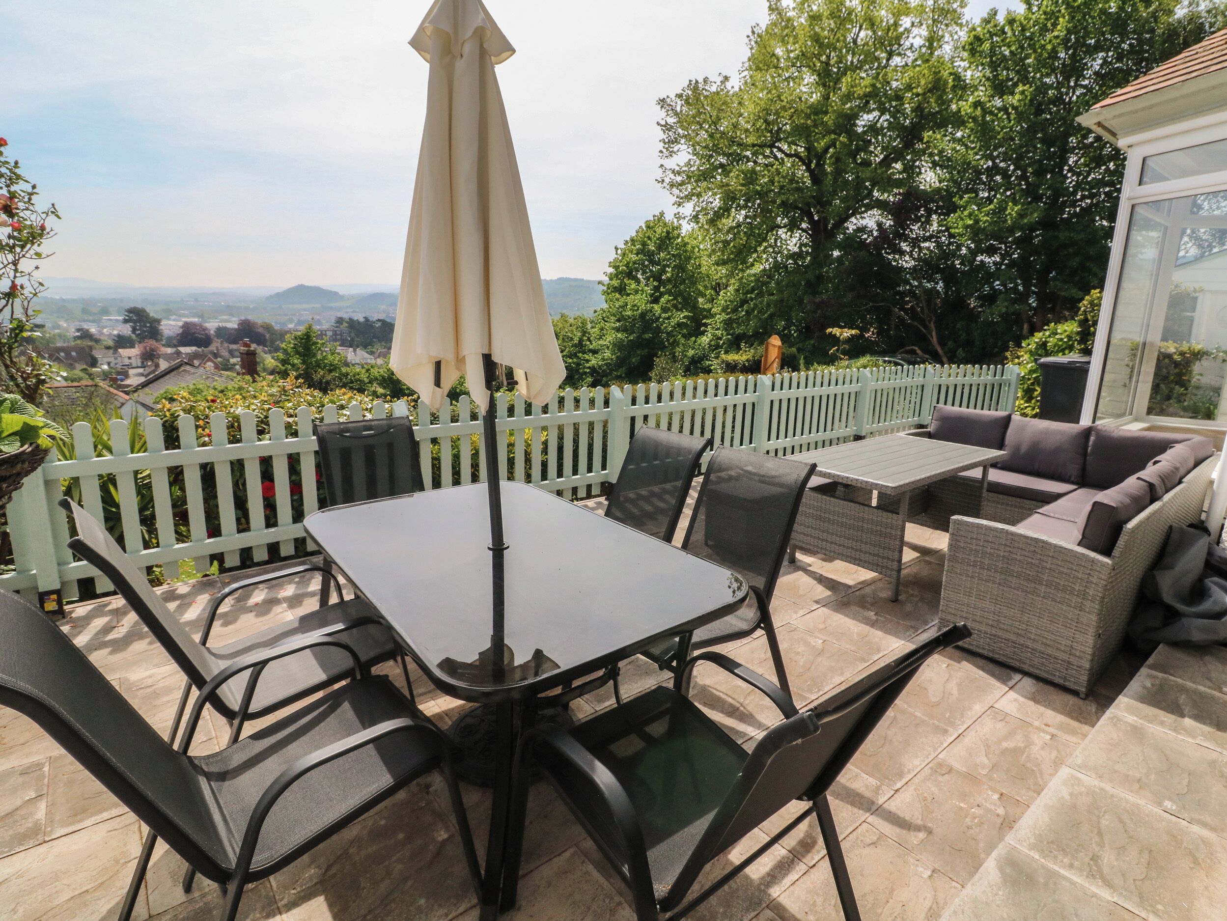 Eine Terrasse im Freien mit Tisch, Stühlen und einer Couch, sowie einem weißen Zaun.