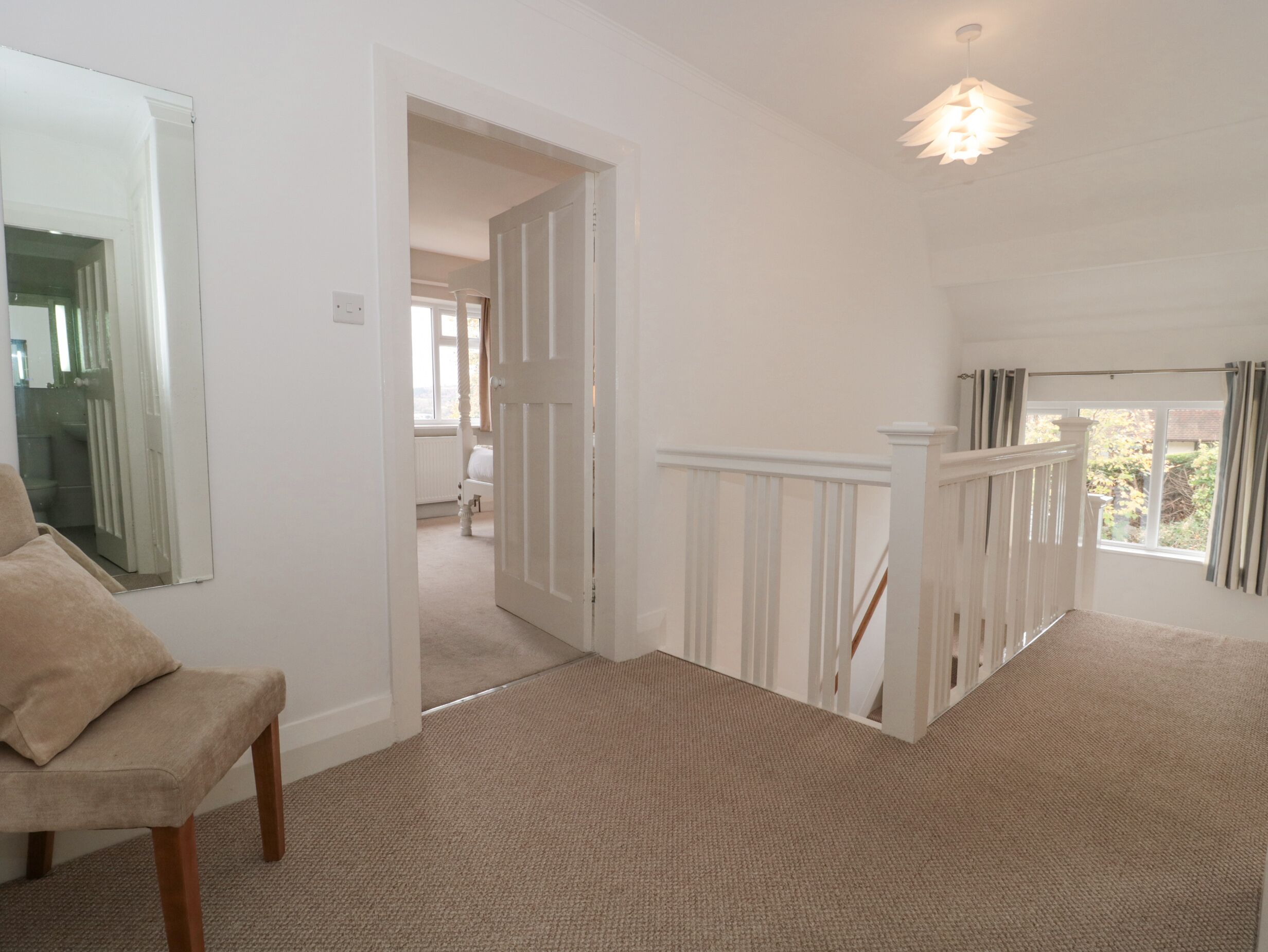 A spacious room with a high ceiling, a large mirror, a beige carpet, and a staircase with white railings leading to another level.