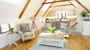 Un dormitorio estilo loft acogedor con techo inclinado, una zona de estar central con una mesita de centro y vistas a la cocina.
