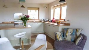 A modern kitchen with white cabinets, a wooden countertop, and a window above the sink. There is a dining area with a glass table and white chairs.