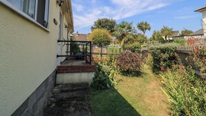 Una propiedad residencial con entrada pavimentada, unos pocos escalones que conducen a una puerta y un jardín con plantas variadas y una cerca.