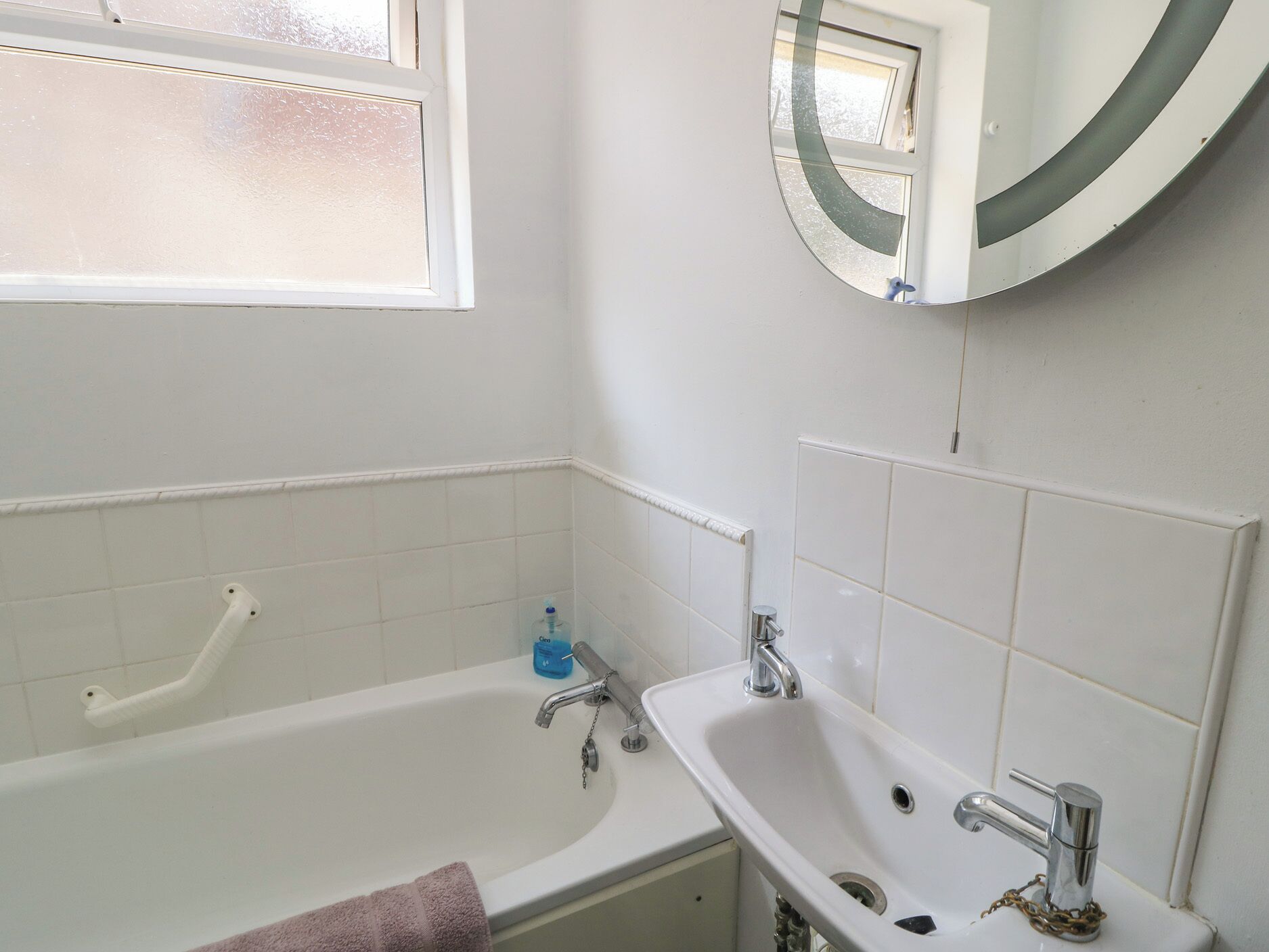 A bathroom with a bathtub, a sink, a mirror, and a window.