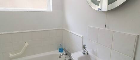 A bathroom with a bathtub, a sink, a mirror, and a window.