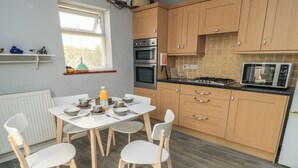 Una cocina moderna con armarios de madera, estufa a gas, horno y microondas. Hay una mesa de comedor con sillas y una ventana encima.