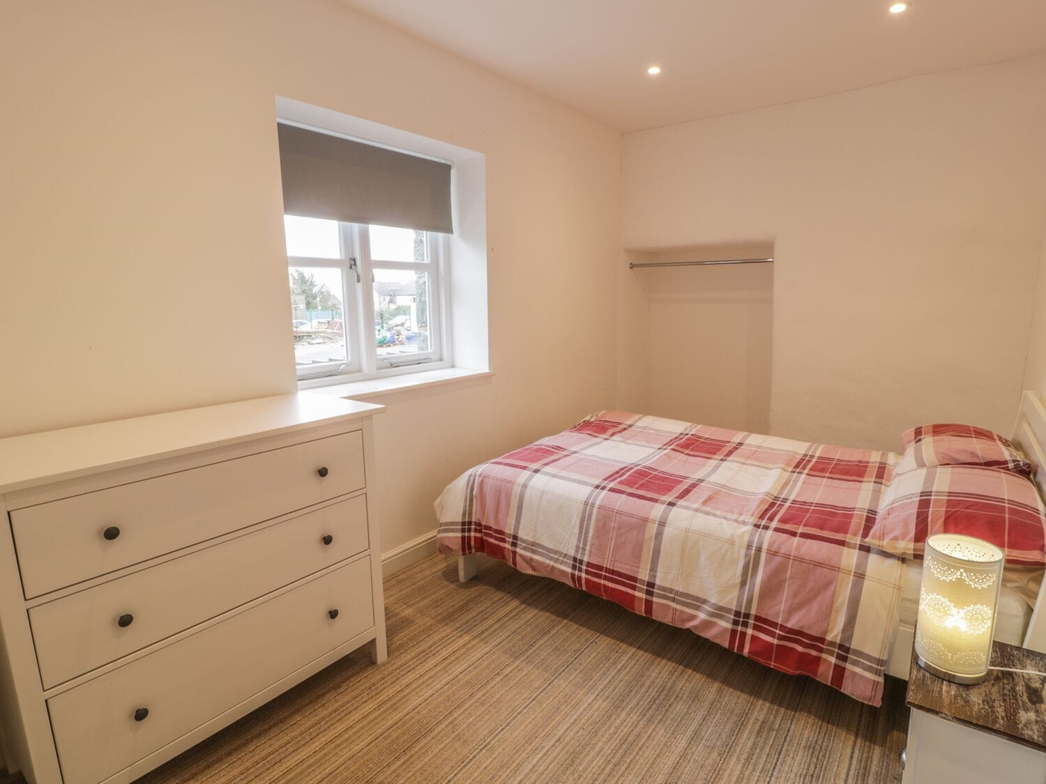 A bedroom with a bed, a dresser, a window, and a bedside table with a lamp.
