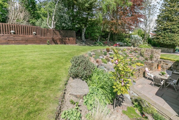 Un jardin bien entretenu, agrémenté d’une clôture en bois, d’un muret en pierre et d’un espace patio avec des meubles d’extérieur.