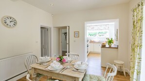 A dining area with a wooden table set for four, white chairs, and a clock on the wall. - St. John's Cottage (Sheffield)