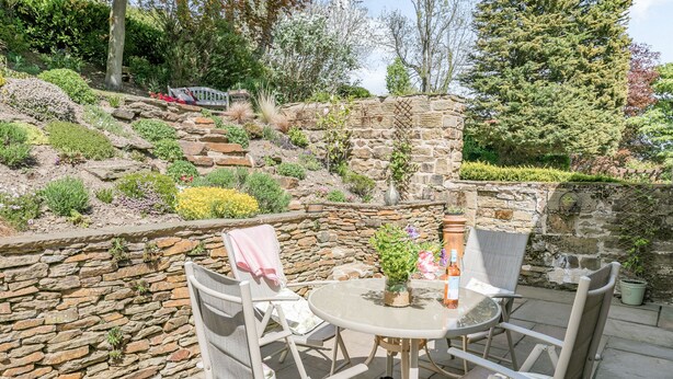 An outdoor patio with a stone wall, a round table, and four chairs. - St. John's Cottage (Sheffield)