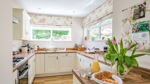 A kitchen with white cabinets, a wooden countertop, a sink, and a window with floral curtains. - St. John's Cottage (Sheffield)