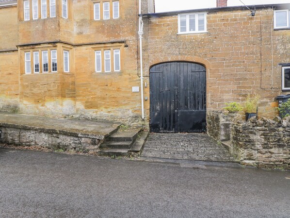 A traditional stone building with a black door, a small set of steps leading to the entrance, and a brick wall with a stone base. - Bower Coach House (Martock)