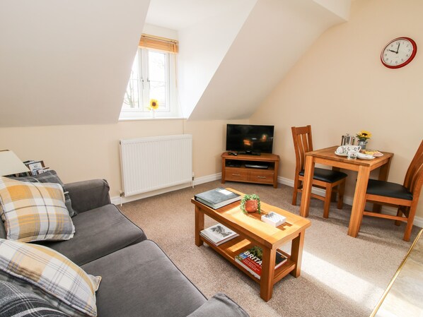 A cozy living room with a sofa, a coffee table with books, a TV, and a dining area with chairs and a table.