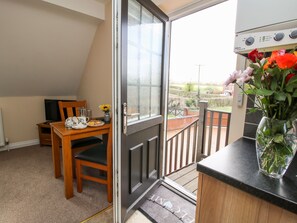 Une pièce comprenant une table à manger, des chaises, un téléviseur et un vase de fleurs sur le balcon.