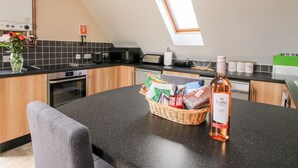 A modern kitchen with a dining area, featuring a black countertop, wooden cabinets, a built-in oven, and a skylight. - The Wynnstead Annexe (Oswestry)