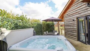 A hot tub in a wooden cabin with a patio area, surrounded by greenery.