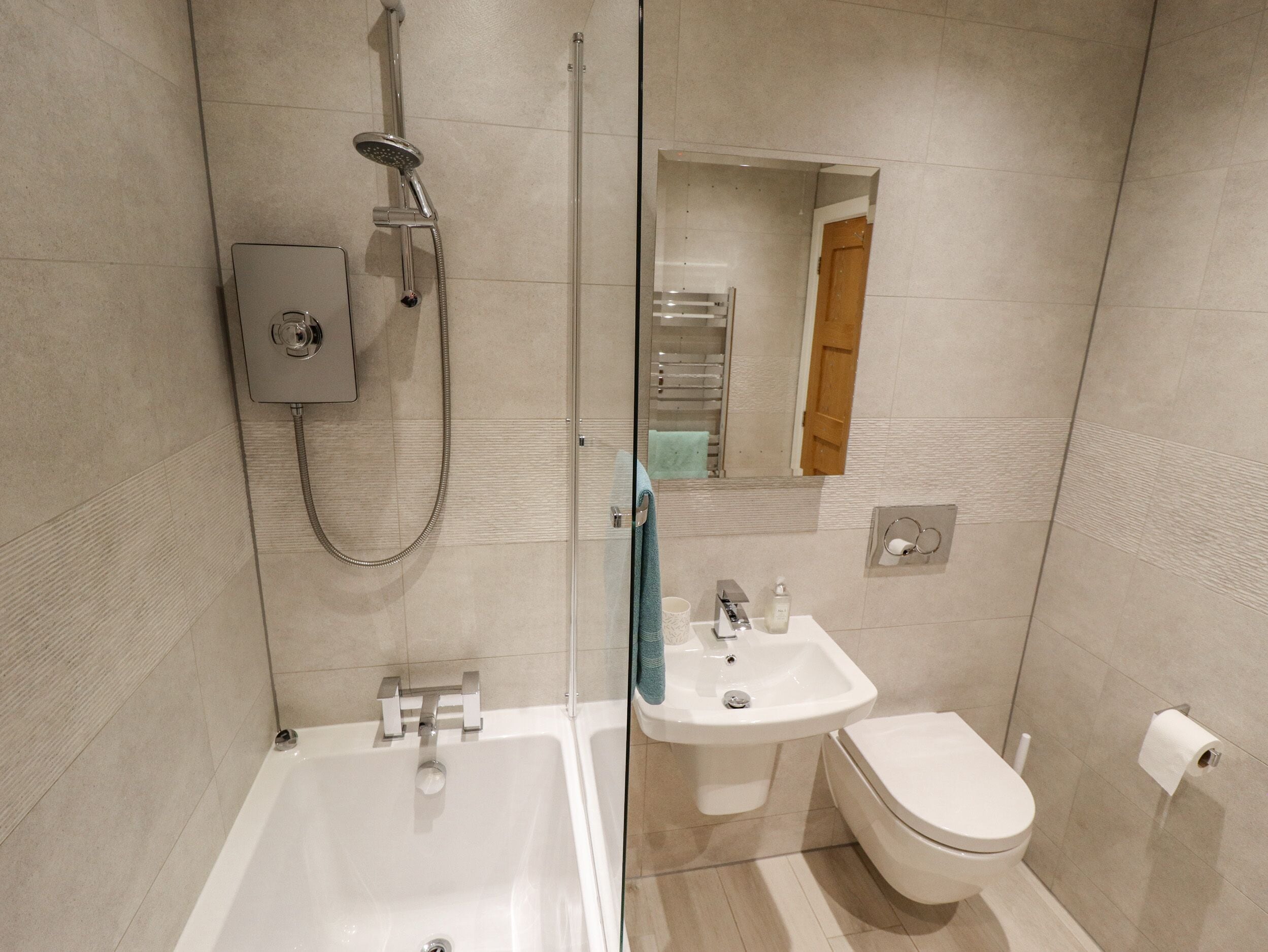 Un baño moderno con ducha de vidrio, bañera blanca, lavamanos y retrete.