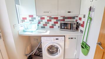 A compact kitchen with a microwave, washing machine, and a small sink.