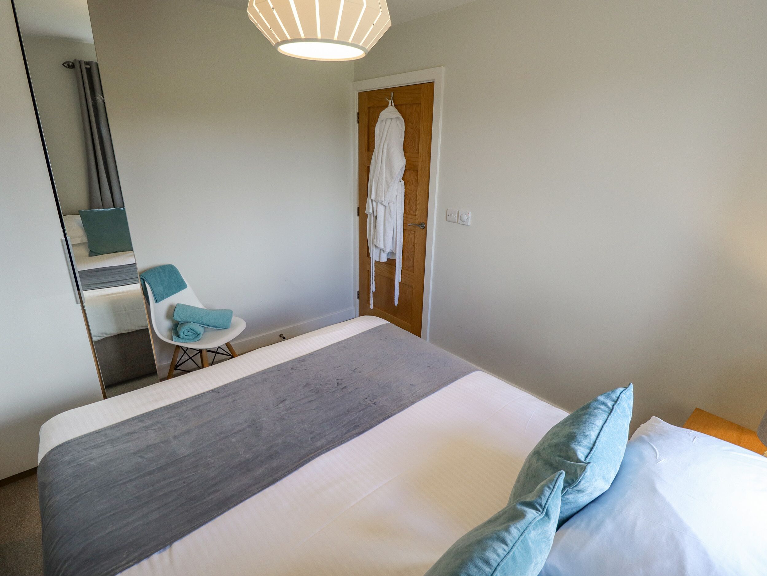 Une chambre d’hôtel avec un lit, une chaise, un peignoir accroché à la porte et un miroir.