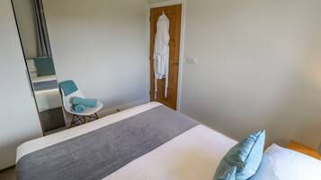 Une chambre d’hôtel avec un lit, une chaise, un peignoir accroché à la porte et un miroir.