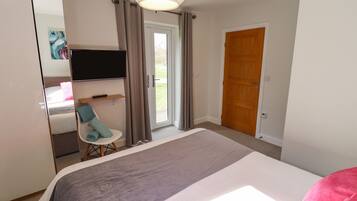 A bedroom with a bed, a TV, a chair, a door, and a window.