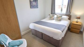 A bedroom with a bed, bedside tables, a chair, a painting, and a window.