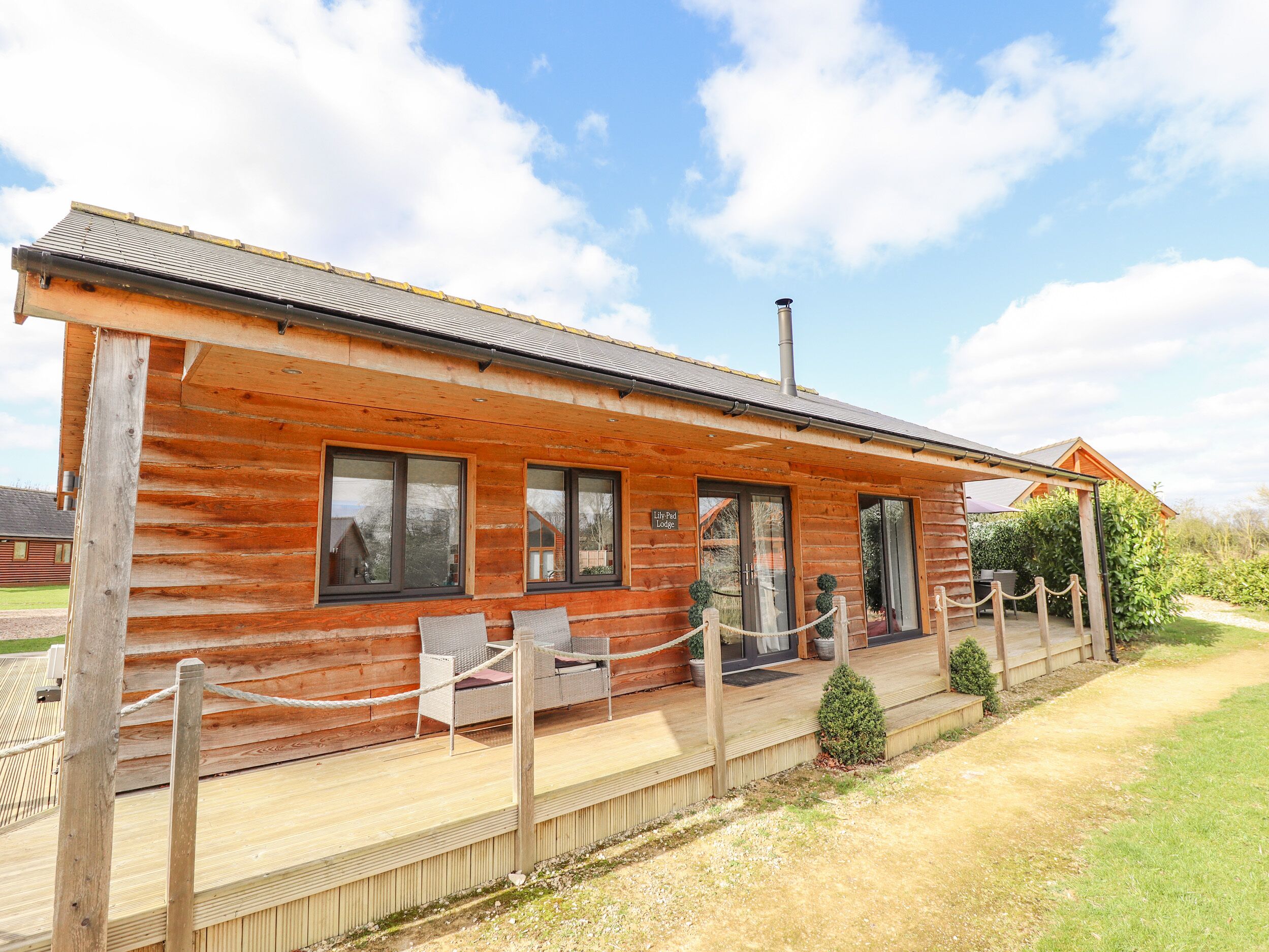 Een houten lodge met een overdekt terras, twee ramen en een bord waarop staat 'Lake Lodge'.