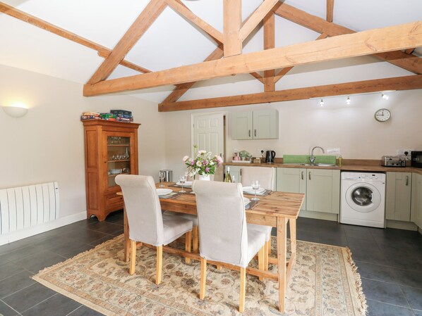 A dining area with a wooden table and chairs, a cabinet with glass doors, a washing machine, and a kitchen area with a sink and cabinets. - Shepherds Burn Cottage (Hexham)