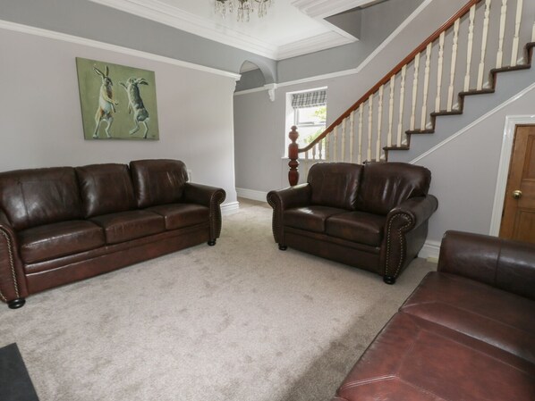 A living room with two brown leather sofas, a wooden staircase, and a painting of kangaroos on the wall. - Dumbuie (Haltwhistle)