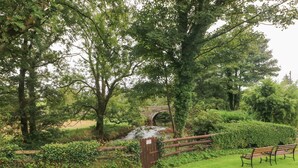 A park with a stone bridge over a stream, surrounded by trees and greenery. - Ty Llwyd (Crymych)