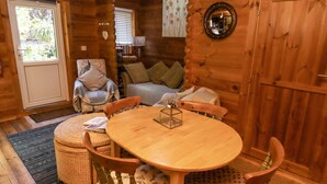 Interior acollidor d'una cabana amb una taula de dinar de fusta, cadires, un sofà i una cadira amb coixí.