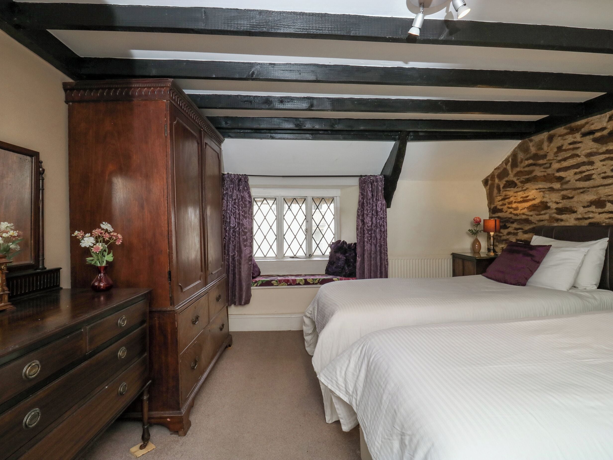 Een slaapkamer met een grote houten dressoir, een bed met witte lakens, een nachtkastje met een lamp en een raam met uitzicht.