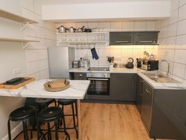 Una cocina compacta con salpicadero de azulejos blancos, electrodomésticos de acero inoxidable y suelo de madera.