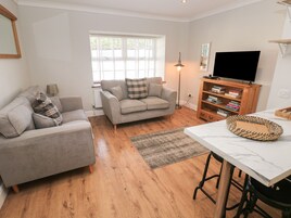 Una sala de estar moderna con un sofá gris, una mesa de centro de madera y un televisor sobre un mueble de madera.