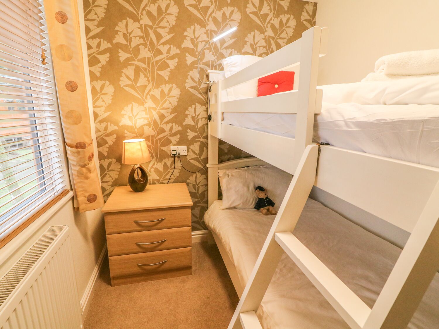 Une chambre avec un lit superposé, une table de chevet, une lampe et une petite commode.