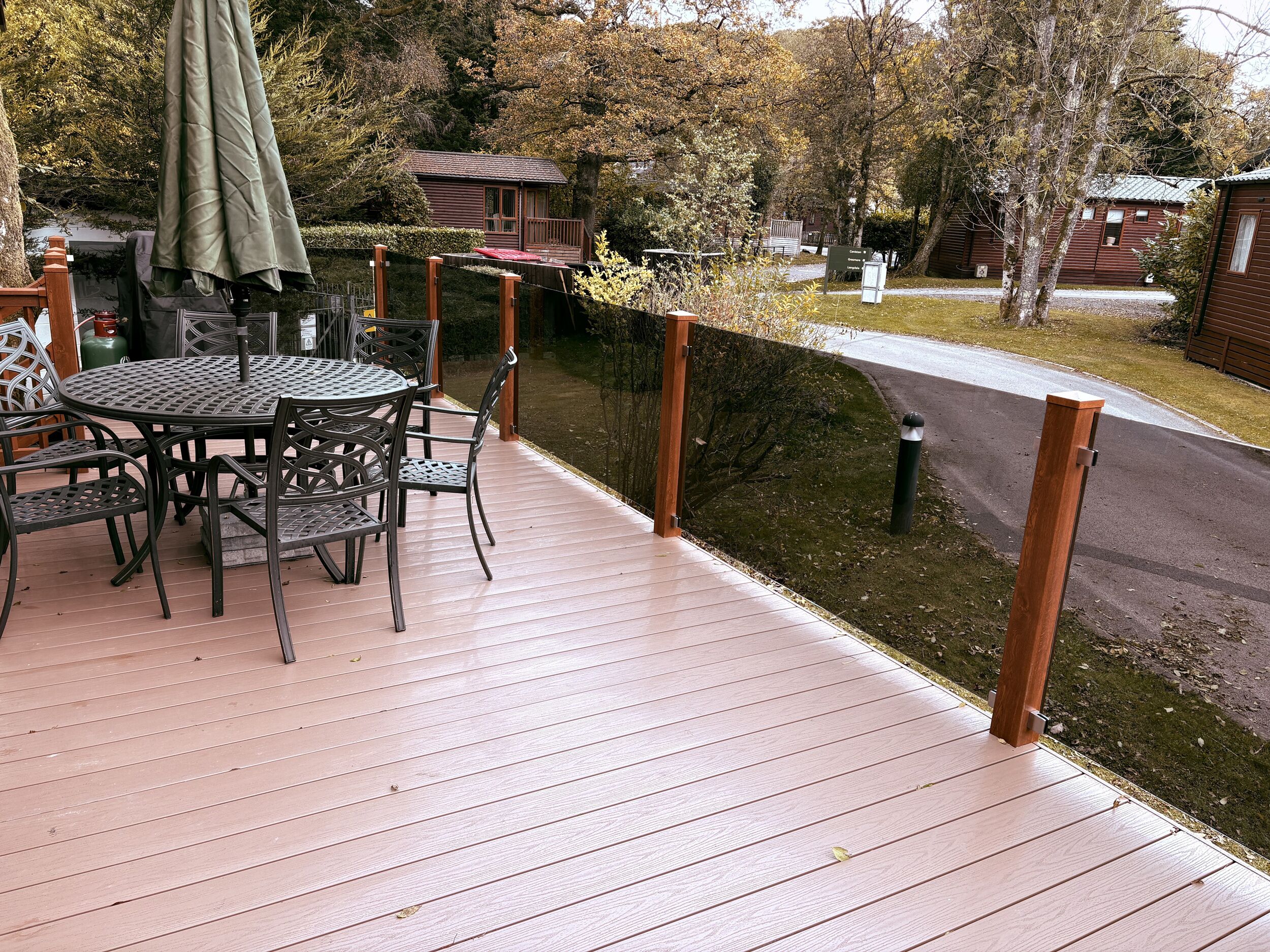 Une terrasse en bois avec une table et des chaises, entourée d’une clôture en bois et d’arbres.