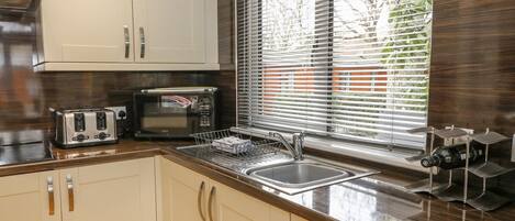 A modern kitchen with white cabinets, a stainless steel sink, a toaster, a microwave, and a window with blinds.