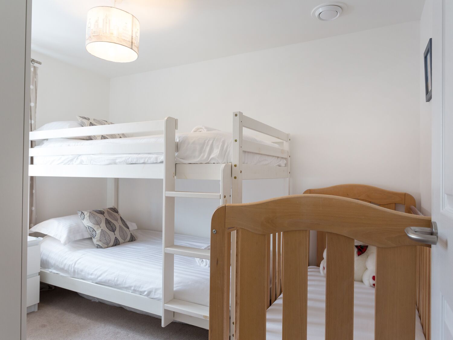 A bunk bed room with a wooden headboard, white bedding, and a hanging light fixture.