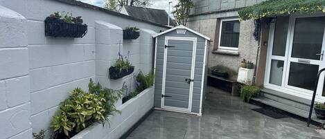 Um pátio com porta cinza, paredes de tijolos brancos e plantas em vasos.