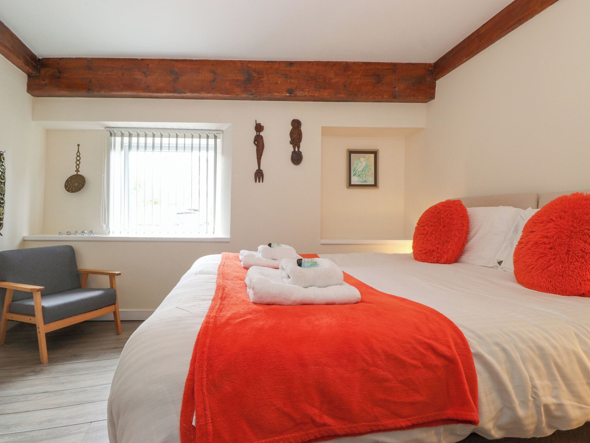 A hotel room with a large bed, a wooden chair, a window with blinds, and a wall with a picture and wall art.