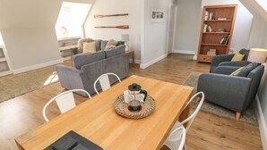 A modern living space with a wooden dining table, grey sofas, and a bookshelf. - North Beach at The Hideaway (Tenby)