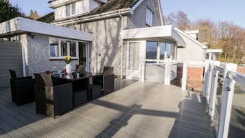 Una casa moderna con una terraza, un área de comedor con mobiliario exterior y un ventanal grande con vistas a la terraza.