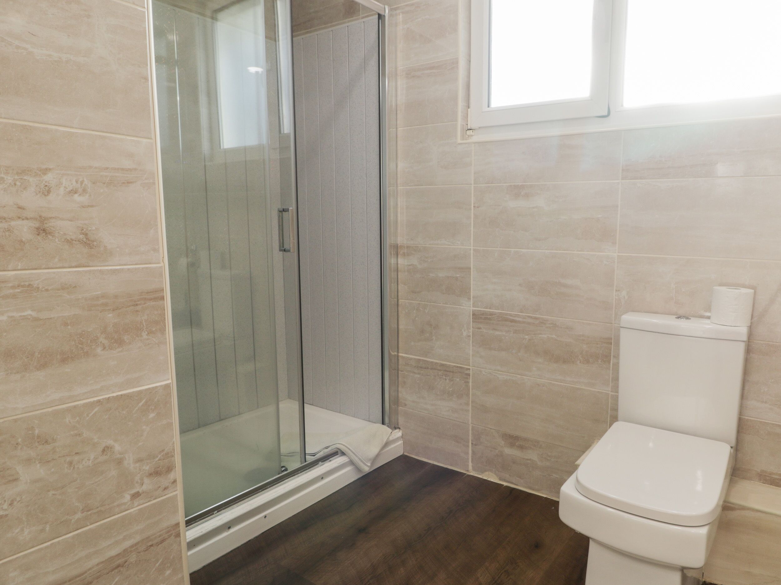 A bathroom with a glass shower enclosure, a toilet, and tiled walls.