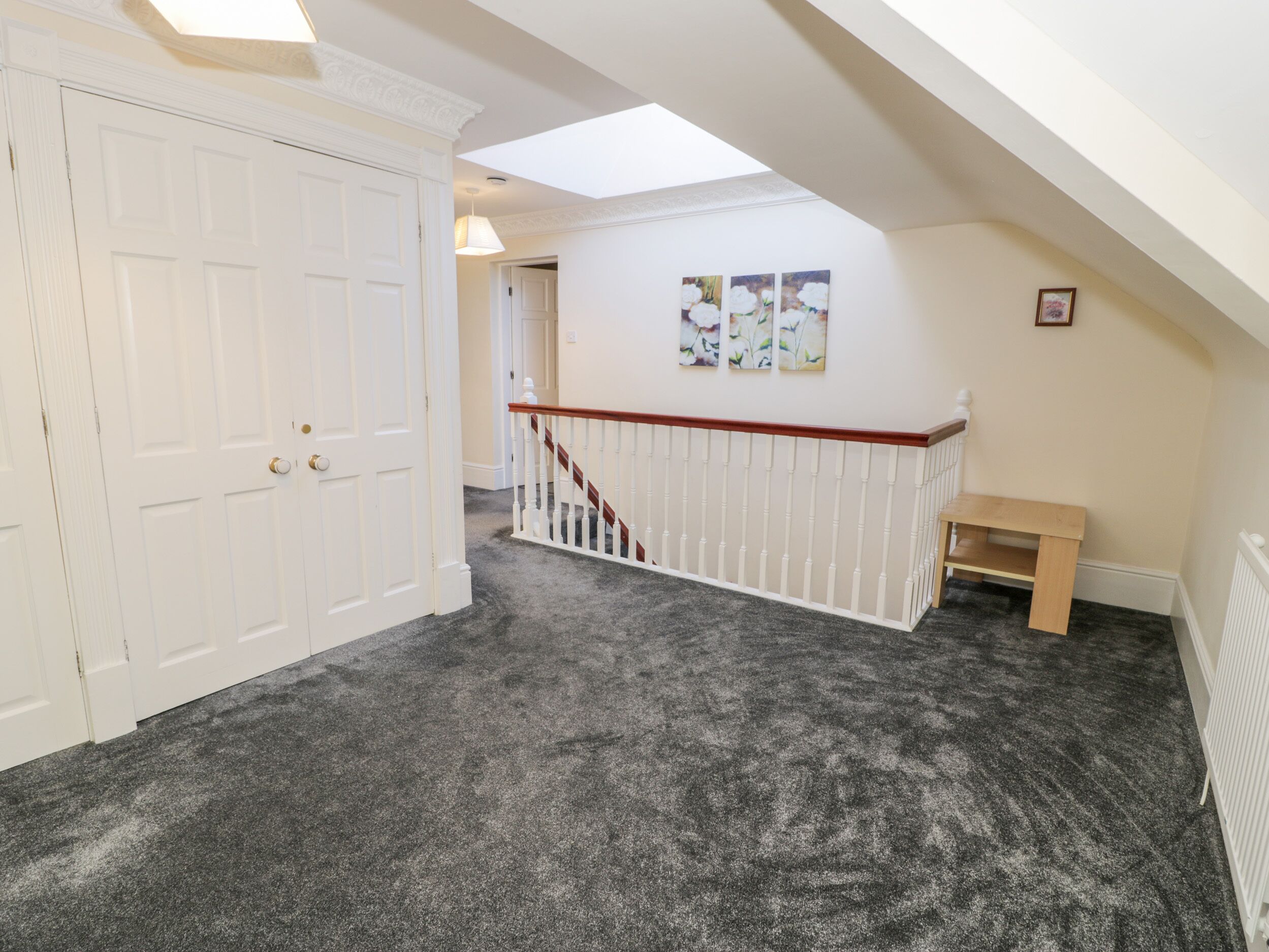A hallway with a carpeted floor, a white door, a staircase with a wooden handrail, and a small bench.