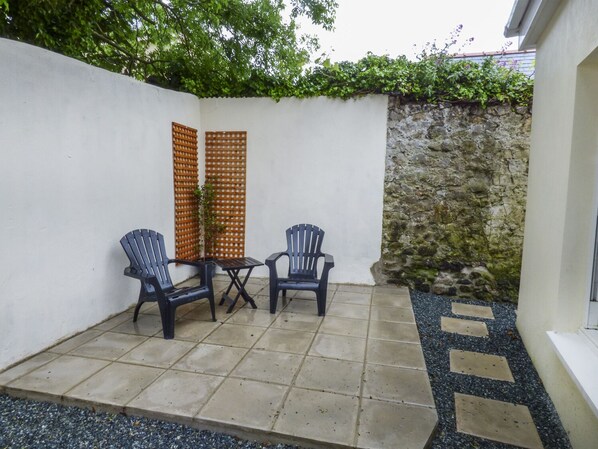 Un patio con dos sillas y una mesa, un muro de piedra y una valla de madera.