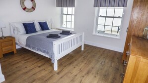 A bedroom with a bed, bedside tables, a hanging life preserver, windows, and a wardrobe. - Harbour Beach at The Hideaway (Tenby)