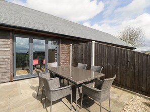 A patio with a table and chairs, a wooden fence, and a sliding glass door leading to an outdoor area. - Rectory Farm View (Yeovil)
