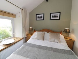 Un dormitorio con cama, dos lámparas de noche, una ventana con vistas y dos cuadros en la pared.
