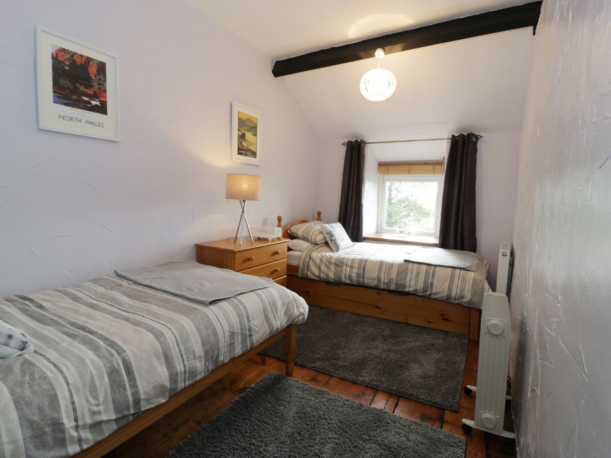 Een slaapkamer met twee bedden, een nachtkastje, een lamp, een radiator en een raam met gordijnen.