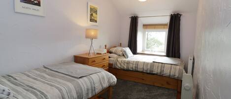 Een slaapkamer met twee bedden, een nachtkastje, een lamp, een radiator en een raam met gordijnen.